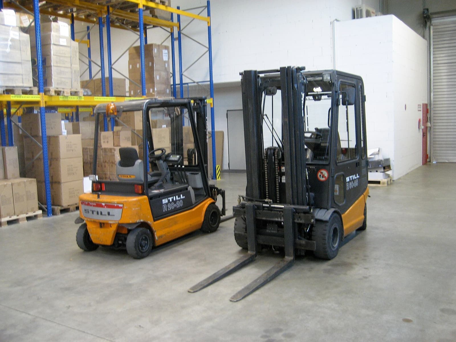 Dua unit forklift elektrik terparkir di lorong gudang